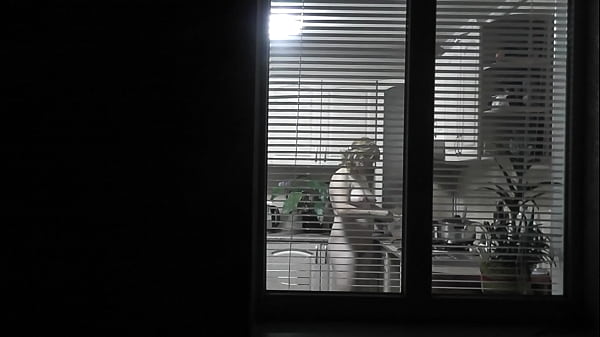Peeping. Watching. Neighbour Pervert Spy View In Evening On Street Looks Out Window As Stripped Sexy Tenant In Kitchen Prepares Dinner For Her Husband. Bare In Public. Stripped At